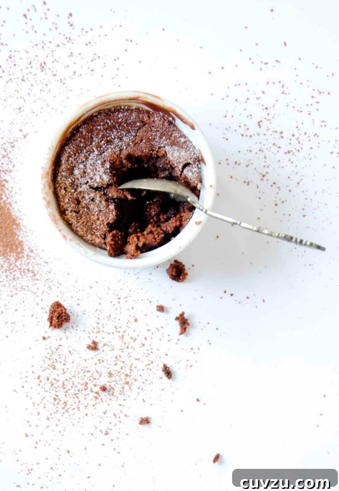 Decadent Chocolate Soufflé 7 A white ramekin filled with a partially eaten double chocolate souffle and a spoon resting inside, showcasing rich layers and airy texture.