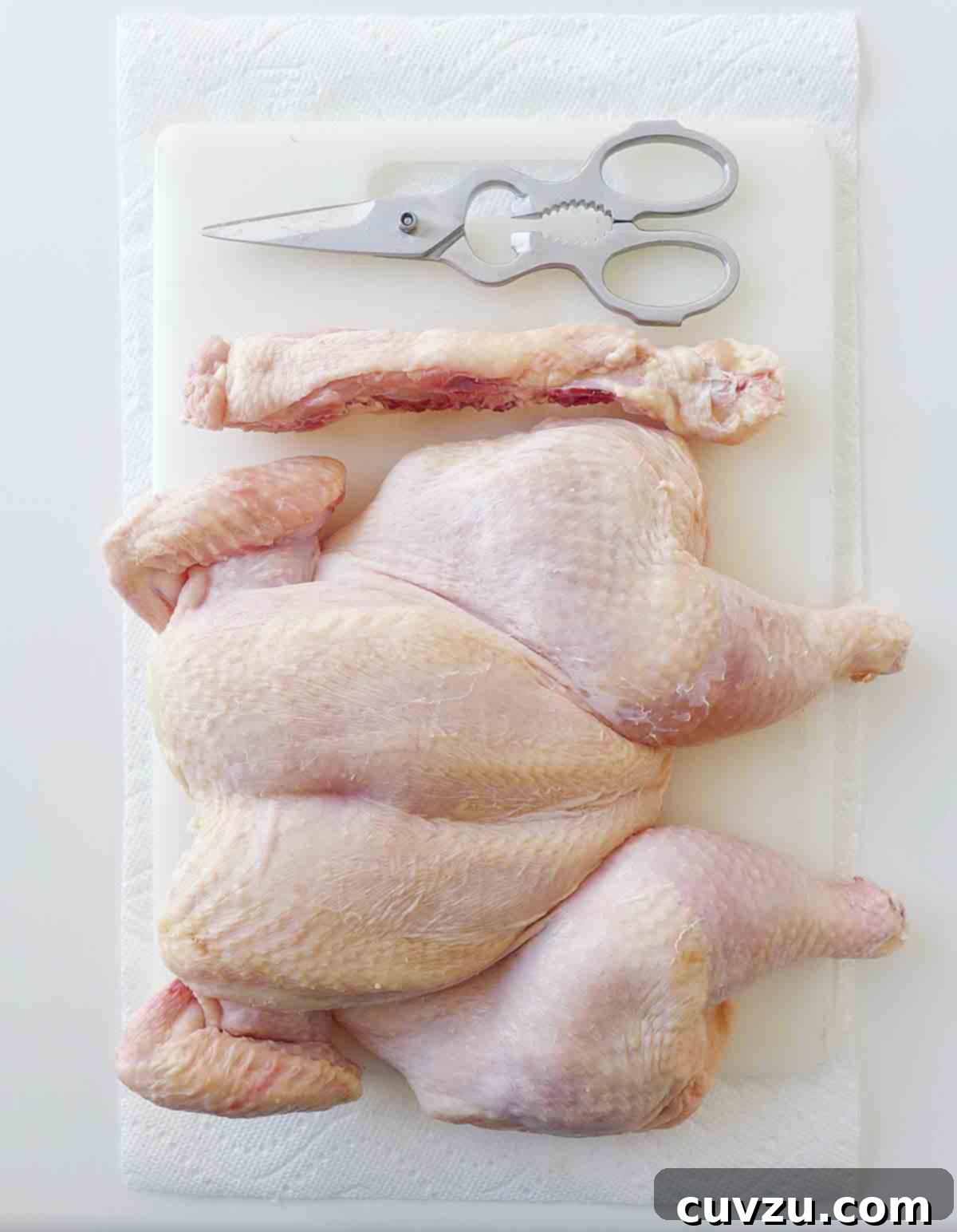 The Art of Spatchcocking 4 A perfectly spatchcocked chicken laid flat on a cutting board, ready for seasoning and cooking, with the removed backbone visible nearby.