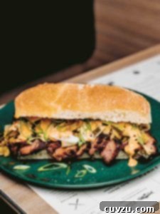 A close-up view of a Kimchi Bulgogi Sandwich, highlighting the rich bulgogi steak, fresh green onions, and mayonnaise inside a toasted bun, presented on a green plate.