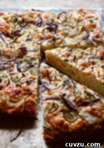Red Onion and Rosemary Focaccia 4 A baked loaf of focaccia with red onion and rosemary with two wedges cut from it.