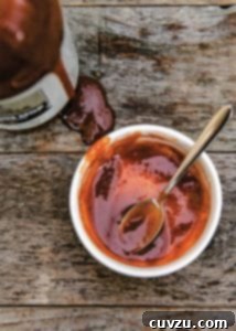 A white bowl with some Memphis BBQ mop sauce and a spoon, with a bottle of the sauce on the side.