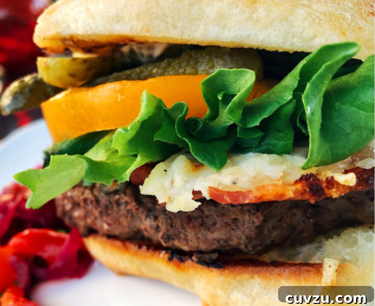 Ultimate Bacon Swiss Burger 6 A beautifully assembled Bacon Swiss Smash Burger, showcasing its juicy patty, melted cheese, crisp bacon, fresh lettuce, tomato, and dill pickle chips on a toasted bun.