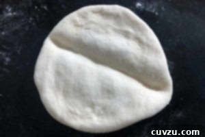 Papo Secos Portuguese Rolls 9 A flattened round of Papo Secos dough with a distinct, deep crease across its center, indicating the next step in the shaping process.
