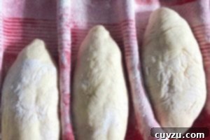 Papo Secos Portuguese Rolls 10 Three unbaked Papo Secos arranged on a ridged, floured kitchen towel, actively proofing before being baked.