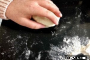Papo Secos Portuguese Rolls 7 A person rolling a ball of dough for papo-secos on a flour-dusted black surface, ensuring a tight, round shape.