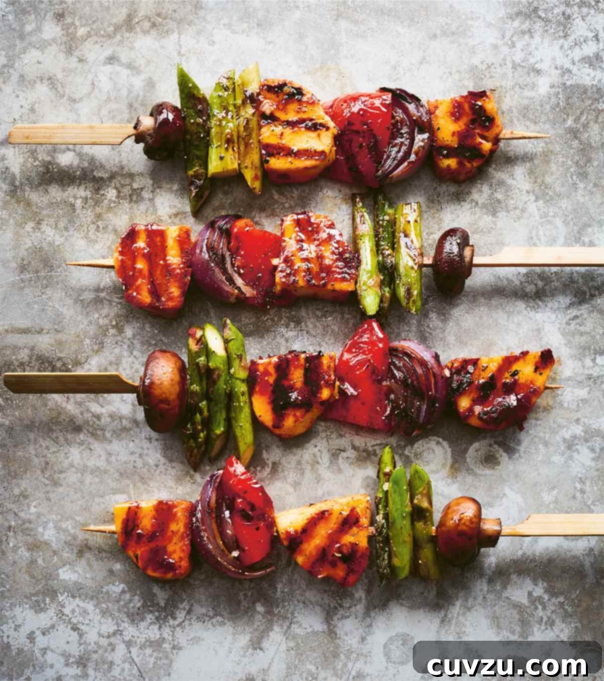 Four grilled vegetable skewers with harissa-marinated halloumi, showcasing colorful vegetables and golden-brown cheese.
