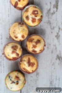Five baked blueberry pecan muffins on a wooden surface.