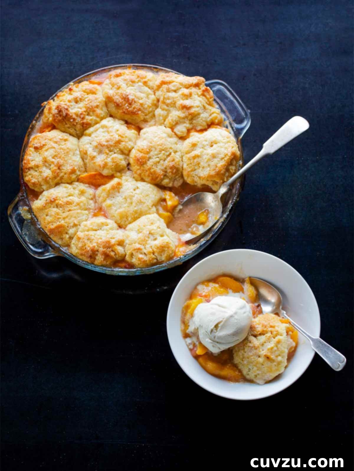 Sun-Kissed Peach Nectarine Cobbler 3 A glass baking dish filled with peach nectarine cobbler with a spoon resting inside, next to a smaller bowl of cobbler topped with a scoop of vanilla ice cream.
