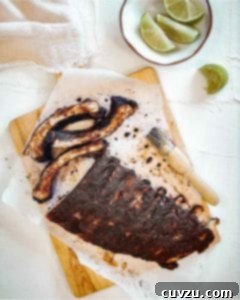 A rack of Vietnamese pork ribs on a sheet of parchment on a cutting board with a basting brush and a bowl of lime wedges nearby.