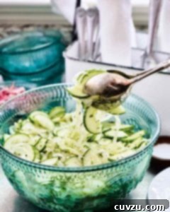 Refreshing Cucumber Onion Medley 3 A serving of cucumber and onion salad being lifted from a serving bowl with silver salad tongs.