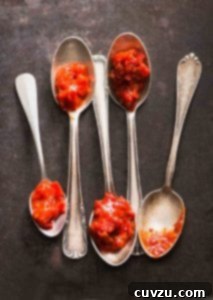 Five spoons, each topped with a dollop of vibrant red Sambal Oelek, a spicy Indonesian chile paste.