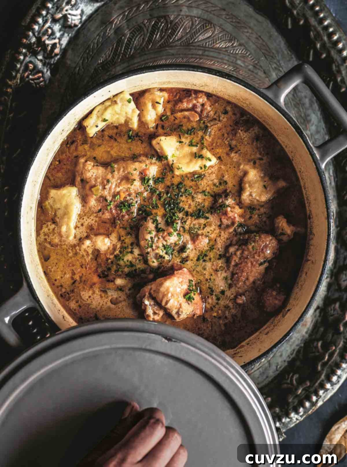 Homestyle Chicken and Dumplings 2 A person lifting the lid off a steaming pot filled with golden chicken and fluffy dumplings.