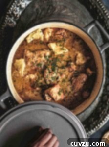 A person lifting the lid off a pot filled with chicken and dumplings.