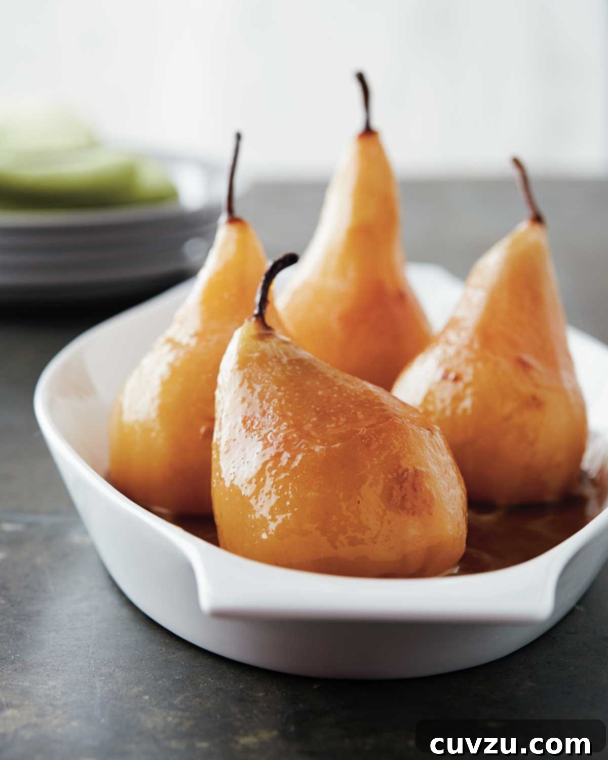 Four wine poached pears in a shallow white baking dish.