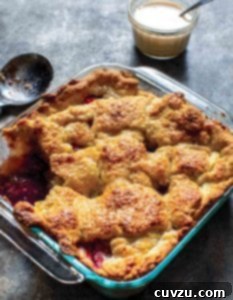 A vibrant peach berry sonker in a square baking dish, with a section removed to reveal the juicy fruit filling and golden pastry crust.