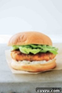 A close-up of a delectable shrimp burger, garnished with tartar sauce and fresh lettuce, served in a classic white bun.