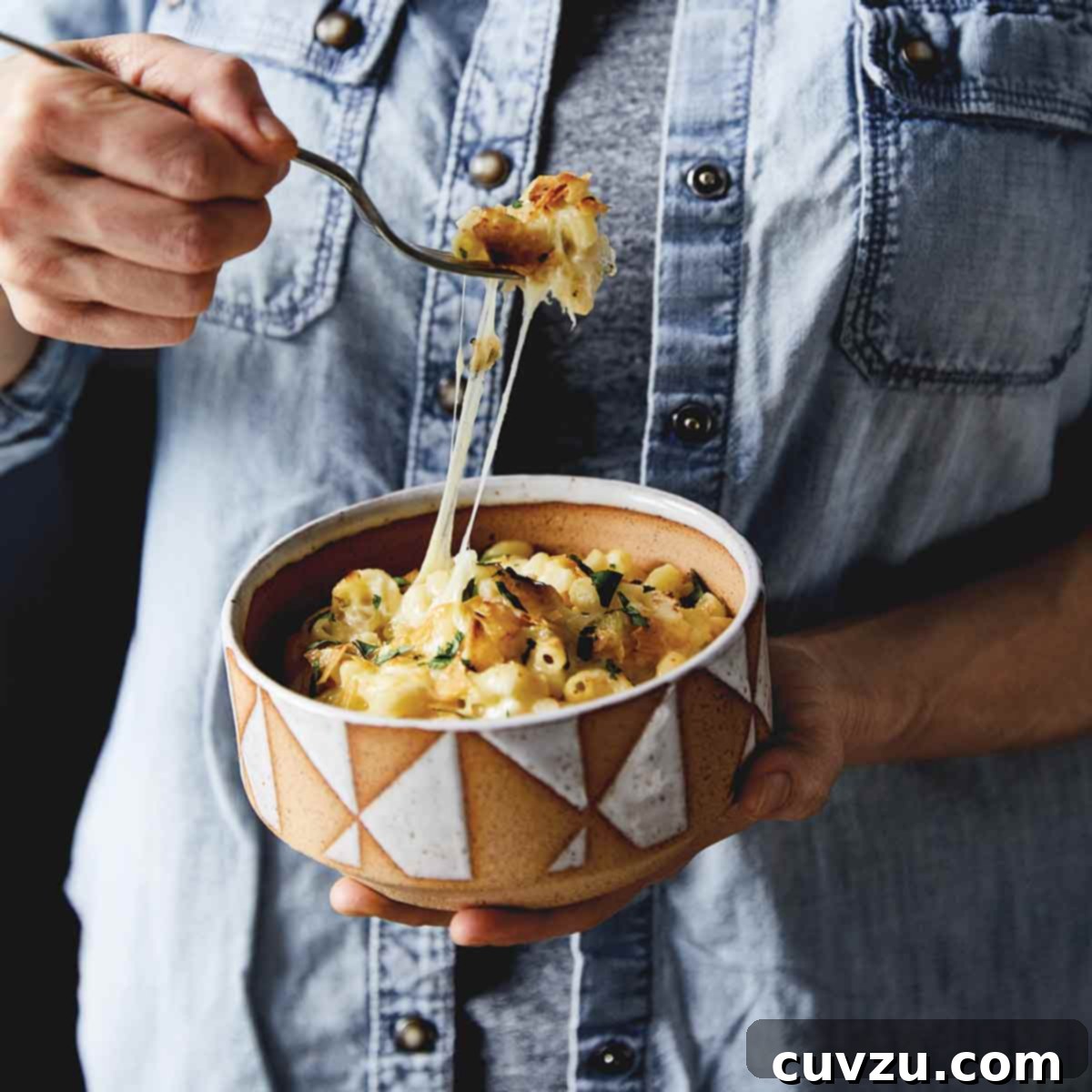 A person scooping a spoonful of green chile macaroni and cheese from a bowl.
