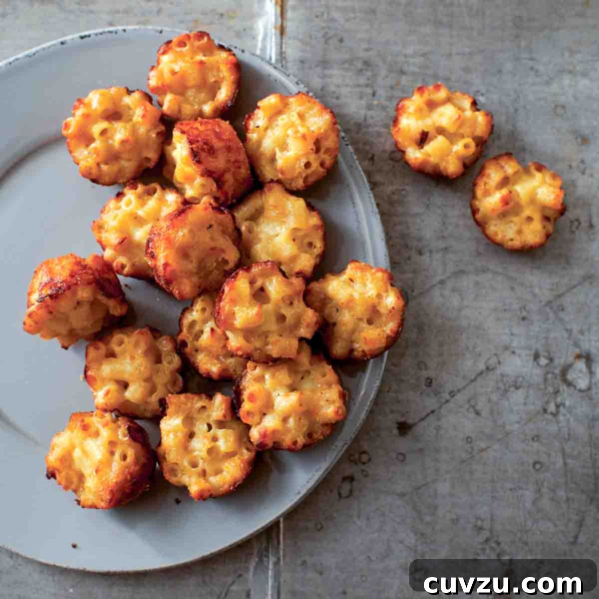 A grey plate half-filled with mac and cheese canapes, with a few resting beside the plate.