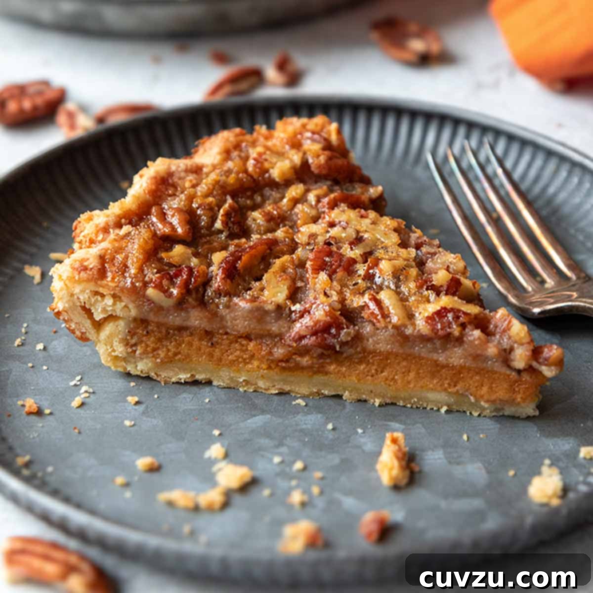 A slice of pumpkin pecan pie on a plate with the remainder of the pie in the background.