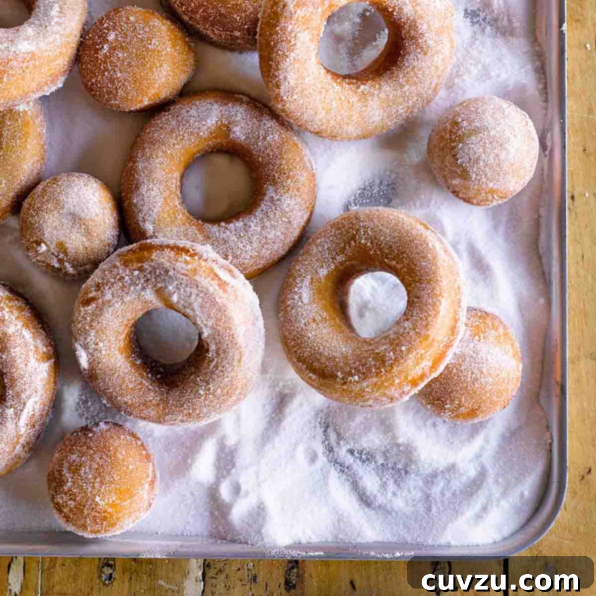 Light Up Your Table: 11 Hanukkah Recipes 8 Easy Jewish Hanukkah doughnuts and doughnut holes covered with sugar, on a metal cookie sheet.