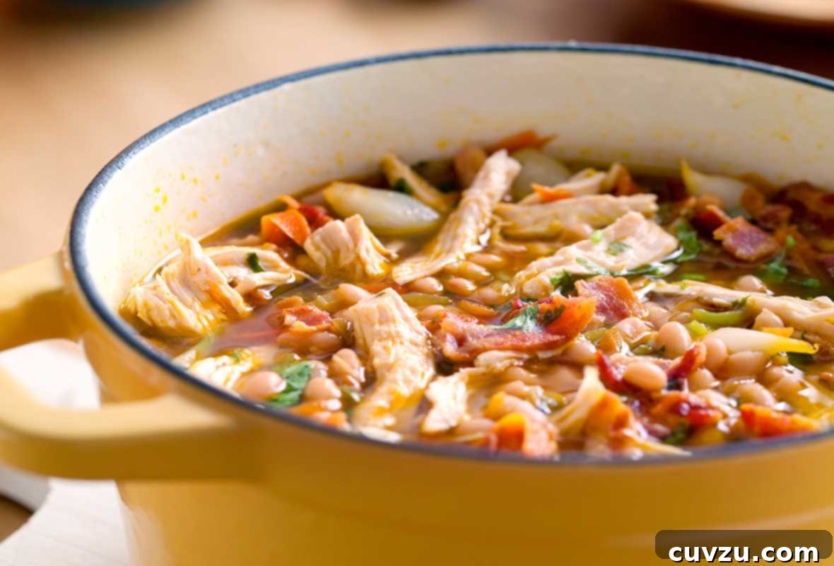 A yellow Dutch oven filled with white bean and chicken chili, topped with pieces of bacon.