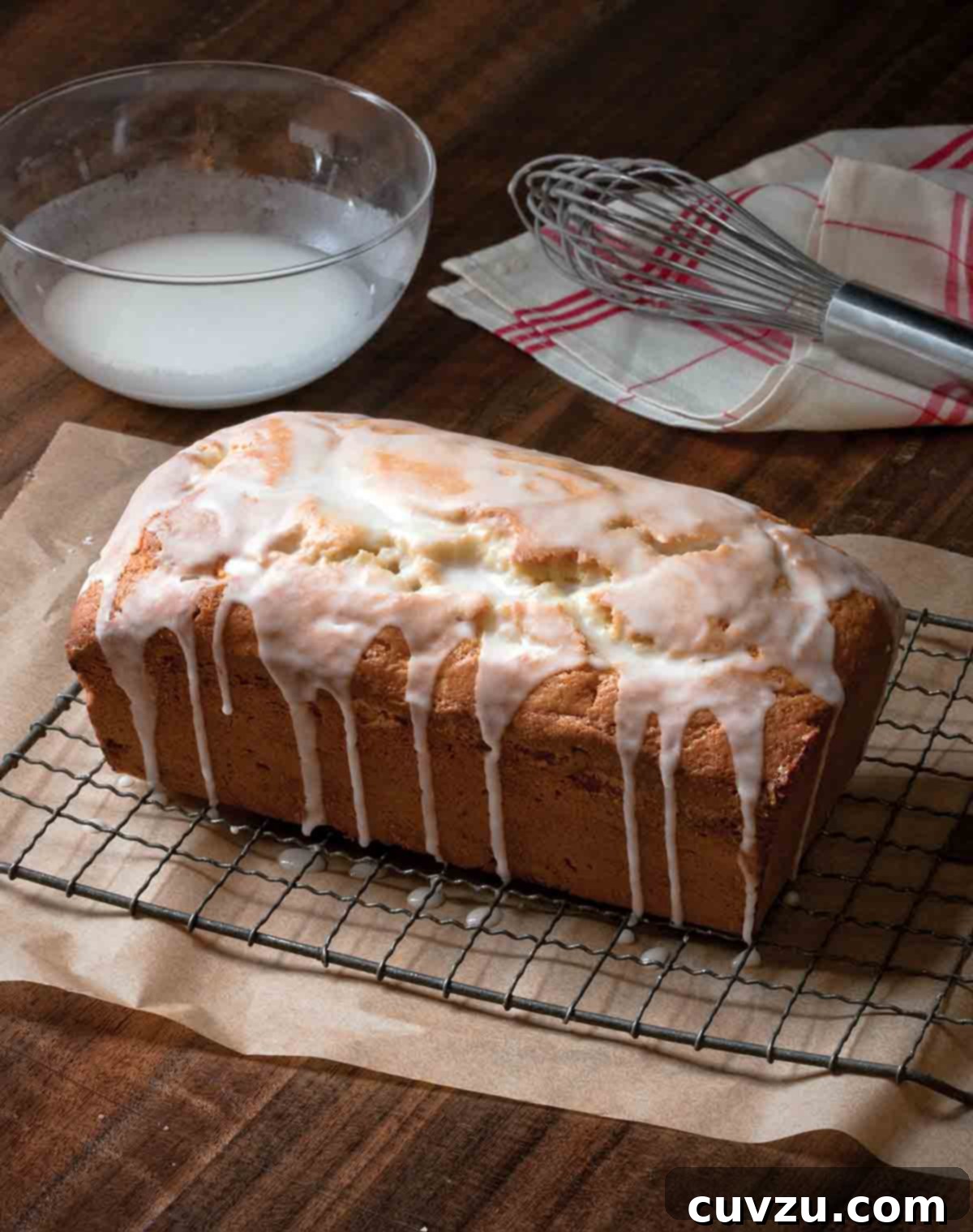Apple Spiced Teacake 3 A beautifully glazed whole apple tea cake resting on a wire rack, with a bowl of lemon glaze and a wire whisk positioned neatly beside it.