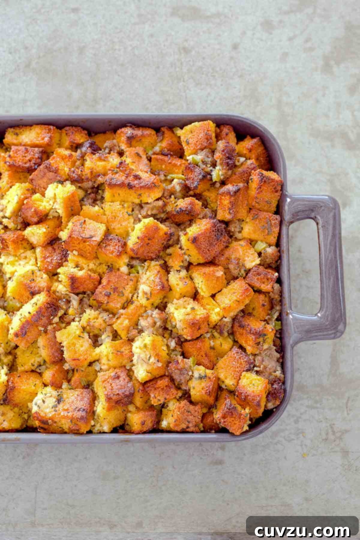 Casserole dish of cubes of homemade cornbread sausage dressing, with pork sausage, onion, celery, and spices.