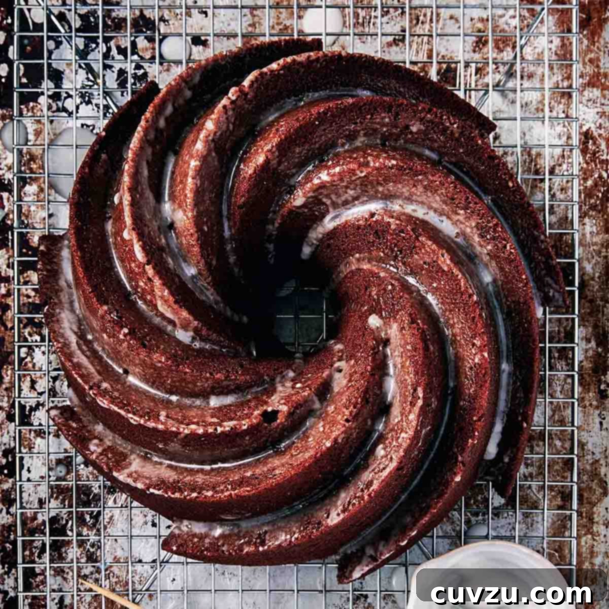 A swirled gingerbread Bundt cake with a lemon glaze on top, all on wire rack over a sheet pan.