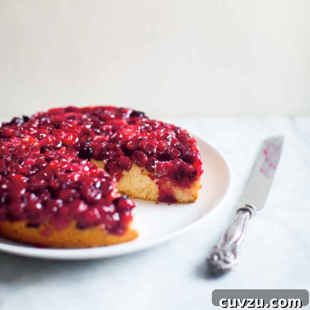 Cranberry upside-down cake with a large piece missing, on a white plate with a serving knife beside it.