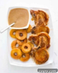 Four French-style pork chops with apples and Calvados sauce on a white platter.