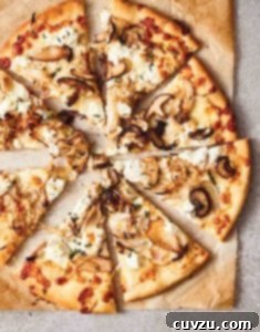 A mushroom pizza with ricotta cut into 8 slices on a piece of browned parchment paper.