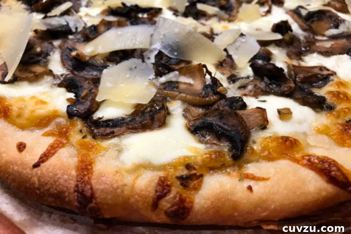 Pillowy Ricotta Mushroom Pizza 6 A baked mushroom pizza with ricotta and shaved parmesan on a sheet of parchment, showing a crispy crust.
