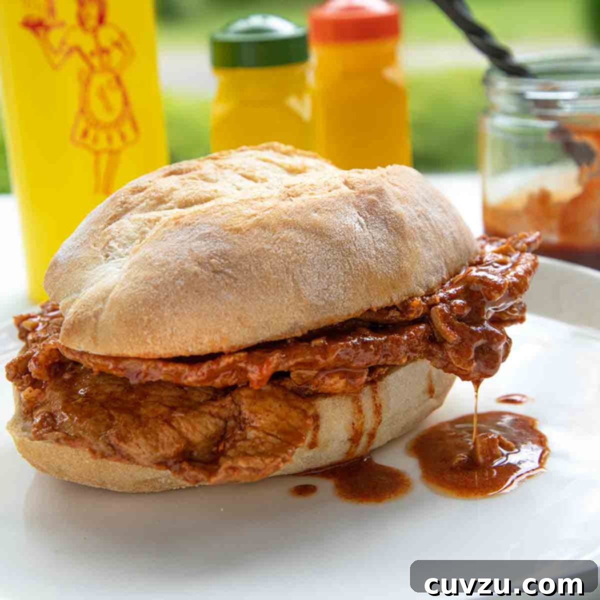 A bifana, a Portuguese pork sandwich on a white plate with a bottle of mustard in the background.