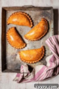 Four curried cauliflower and potato pasties in a metal baking dish with a pink and white striped towel on the edge.