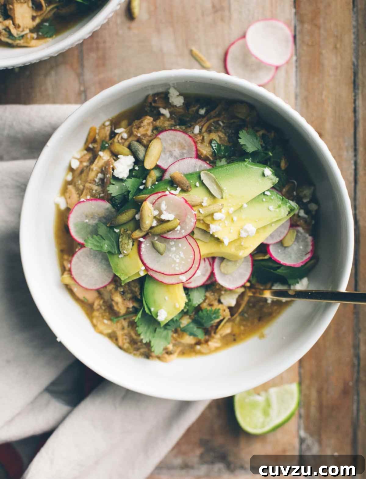 A white bowl filled with pozole verde, topped with sliced radishes, pepitas, avocado, and cilantro.