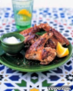A green plate topped with a few garlicky chicken wings, a bowl of salt, and a lemon wedge.