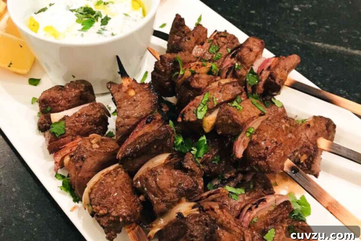 Effortless Sheet Pan Beef Skewers 4 Sheet pan beef skewers piled on a white rectangular serving platter with a white dip and lemon wedges.