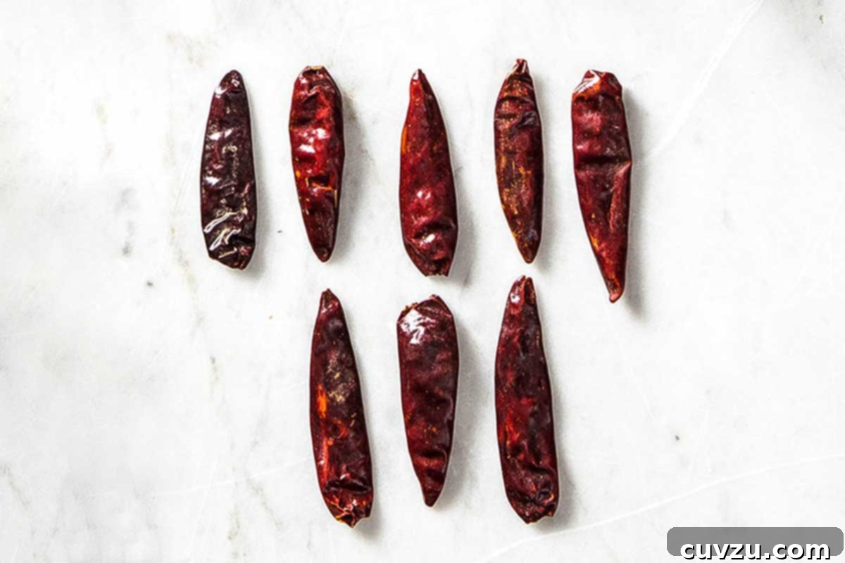 Demystifying Dried Chile Varieties 7 A cluster of eight small, vibrant red dried Calabrian peperoncini chile peppers, indicating their potent heat and fruity essence.