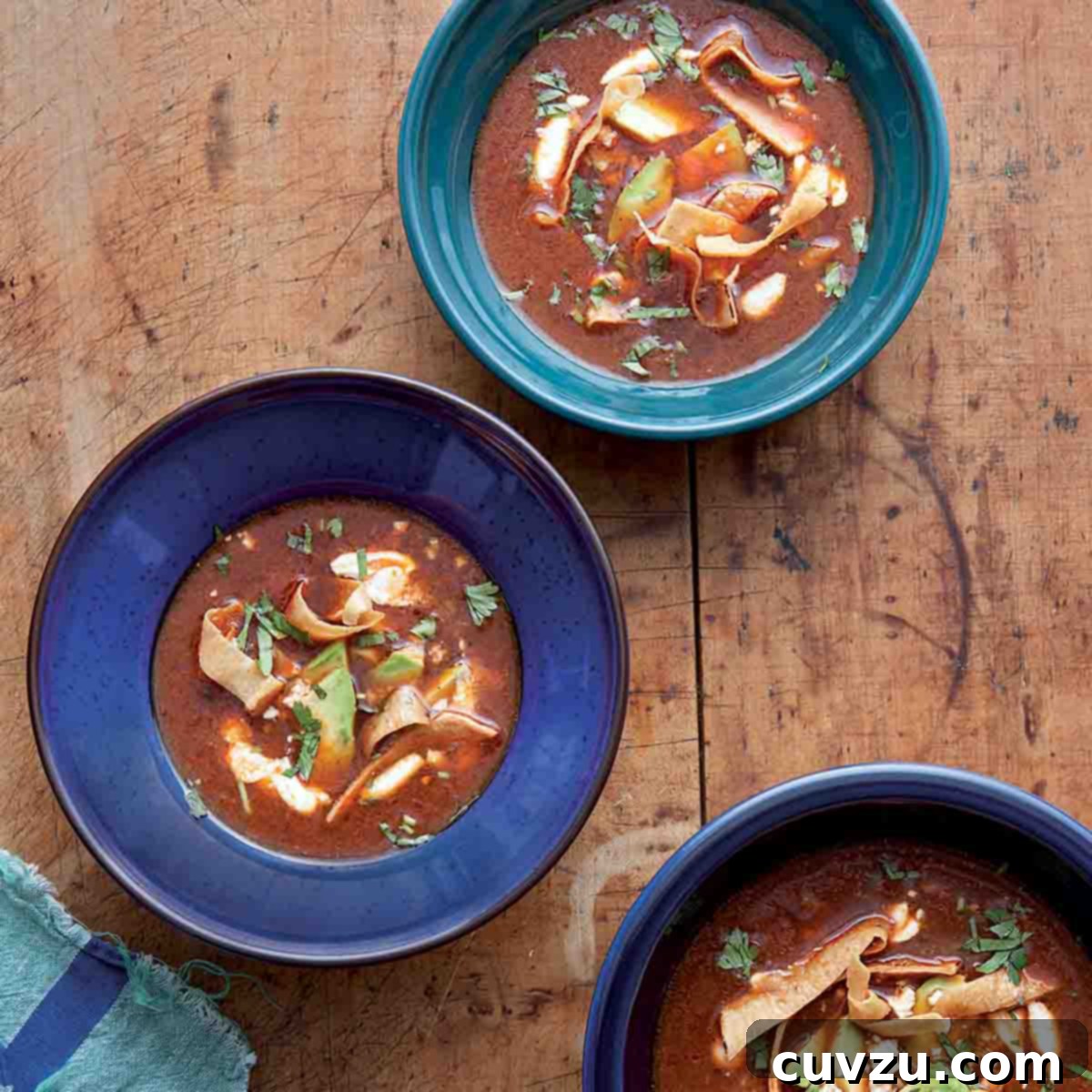 Three blue bowls filled with ancho chile soup on a wooden table.