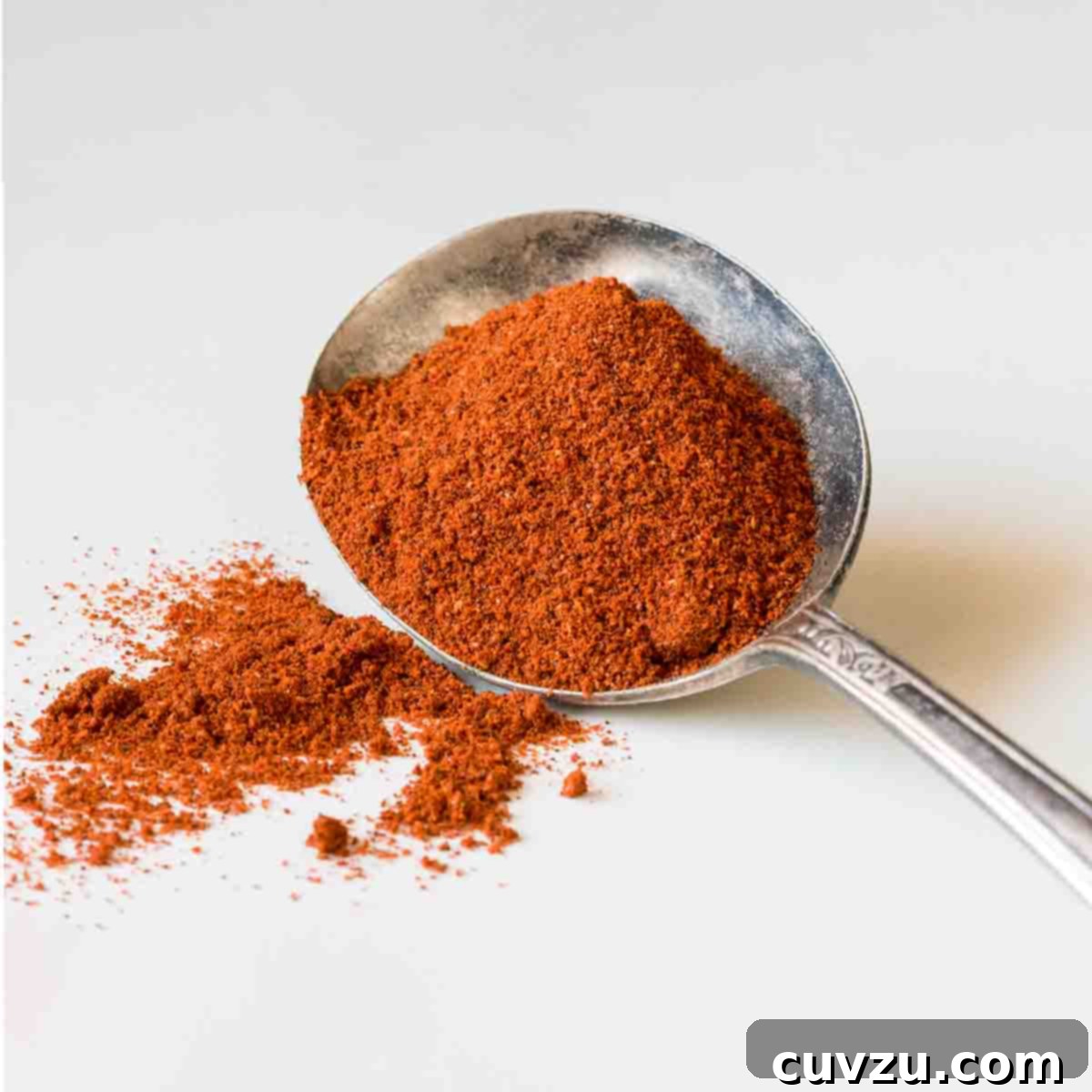 A large silver spoon holding a scoop of homemade chili powder with some spilled on the side.