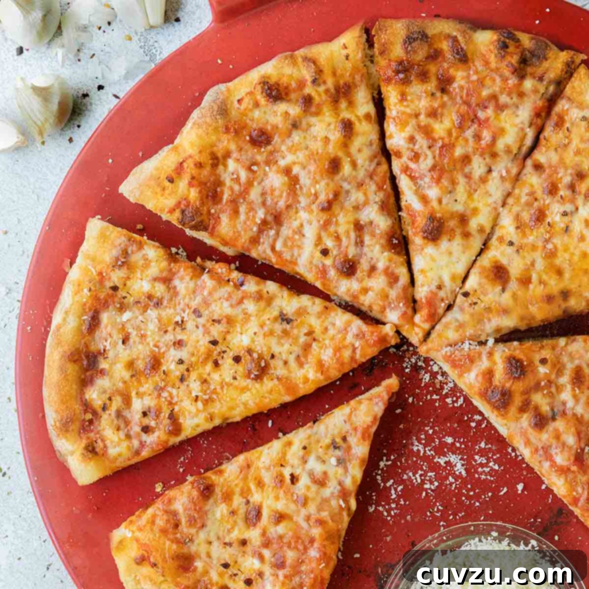 A New York-style pizza sliced into 8 pieces, with one slice missing and a bowl of parmesan on a red pizza plate.