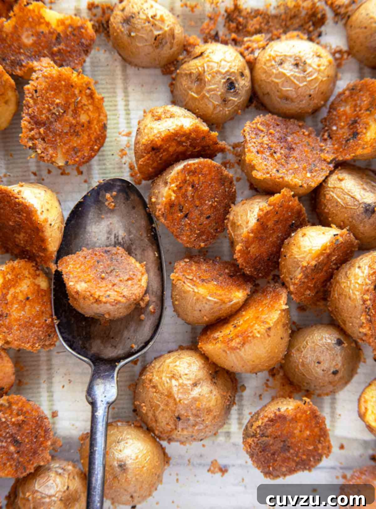 Savory Golden Parmesan Potato Bites 4 Crispy herbed Parmesan potatoes on a white cloth and one resting on a spoon.