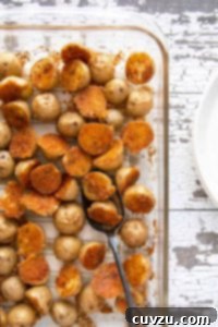 Savory Golden Parmesan Potato Bites 5 A baking dish filled with crispy herbed Parmesan potatoes on a white wooden surface with white plates beside it.