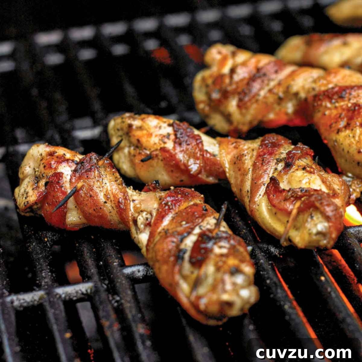 Several glistening bacon-wrapped chicken wings arranged on a hot grill grate with embers glowing underneath, showcasing their crispy texture.