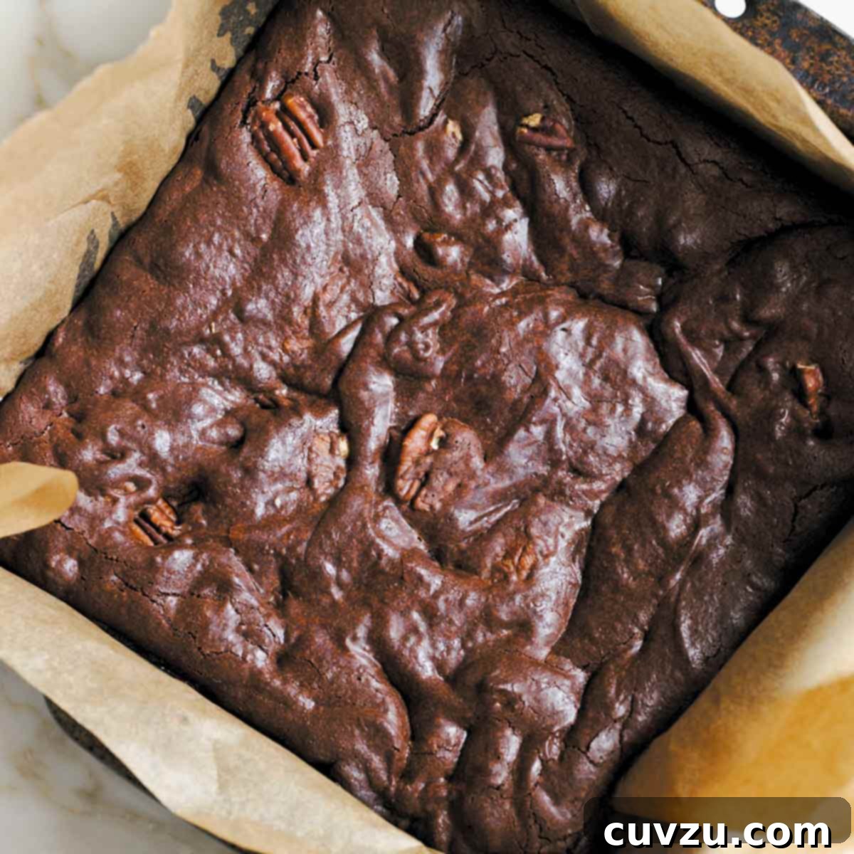 A parchment-lined square pan filled with pecan-studded best brownies.
