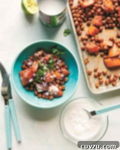 A bowl of roasted sweet potatoes and chickpeas, garnished with cilantro, next to a sheet pan and a bowl of coconut milk.