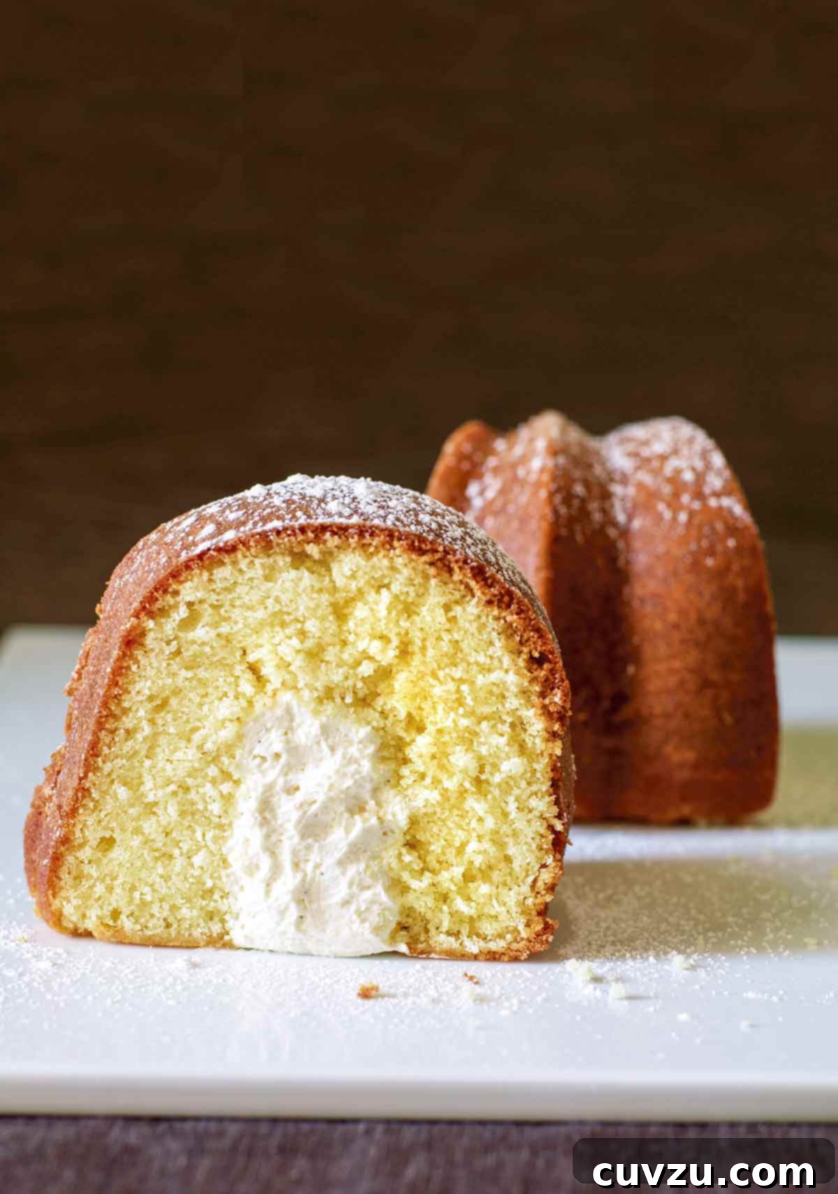 A slice of Twinkie Bundt cake dusted with confectioners' sugar and turned to show the cross section of its cream-filled interior.