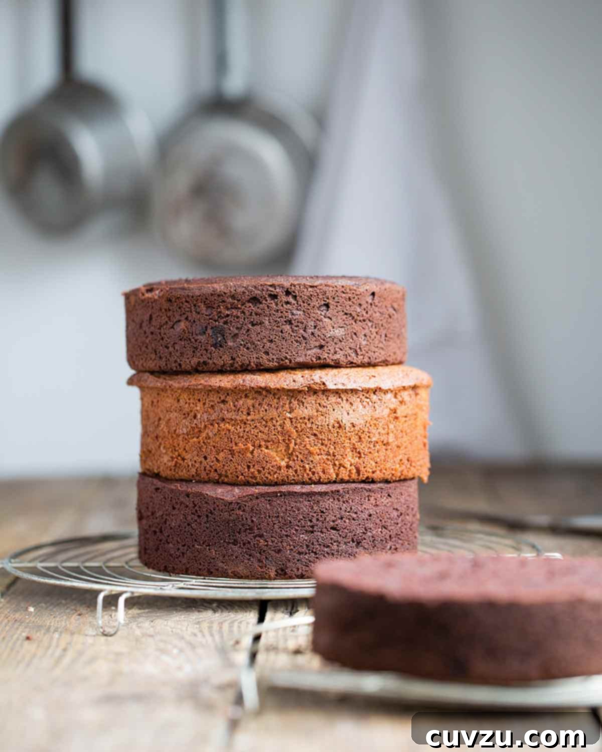 A paleo vanilla cake stacked between two chocolate cakes on a wire rack.