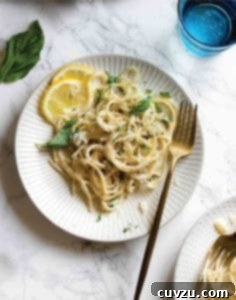 Two white plates topped with lemon basil pasta with lemon slices on the side and a gold fork resting on the side of each plate.