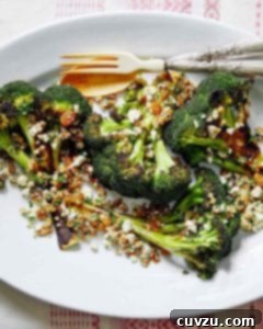 A white oval plate topped with broccoli with walnuts, raisins, and ricotta salata with a fork and spoon on the side.